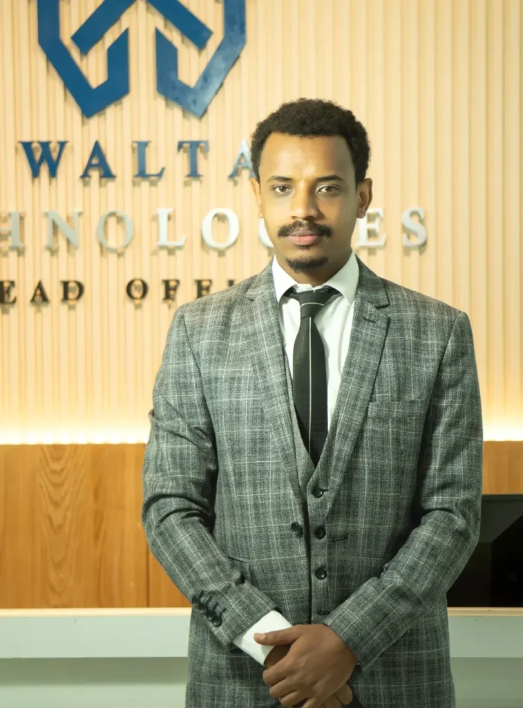 Walta Technologies Marketing Manager standing in the company's headquarters reception area wearing a gray business suit.